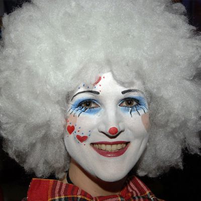 Eine Person mit weißer Perücke und bunter Schminke lächelt fröhlich während der Weiberfastnacht-Proklamation.